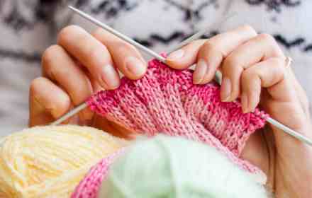 Image of knitting needles and hands creating some knitwear