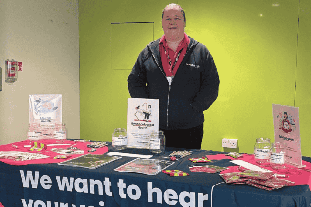 image of emmy our senior engagement officer at Lancaster and Morecambe college infront of a table with Healthwatch leaflets and posters on