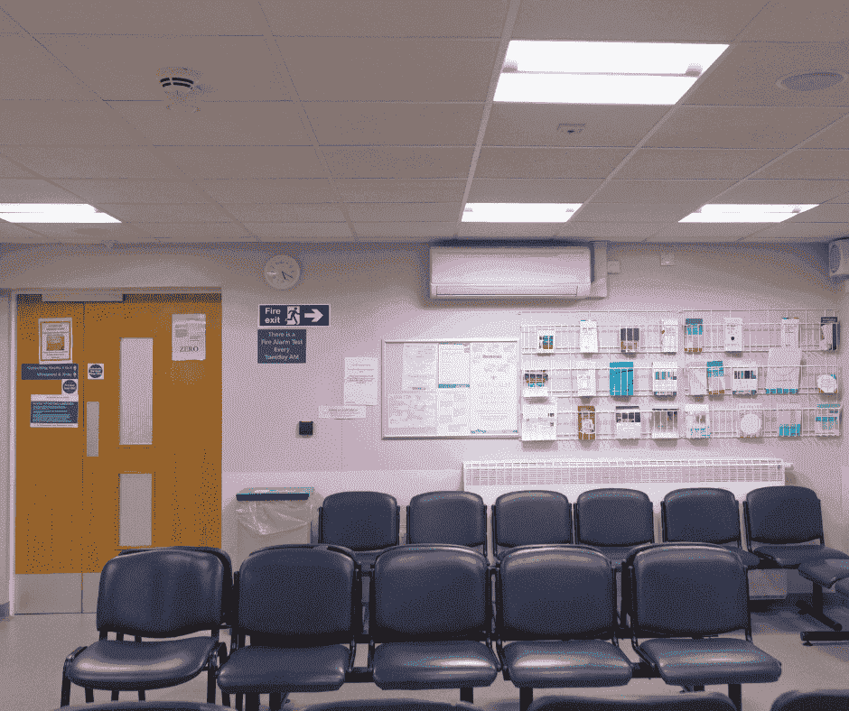 Image of a waiting room that could be in a hospital, or GP with rows of chairs and health related leaflets on a purple wall